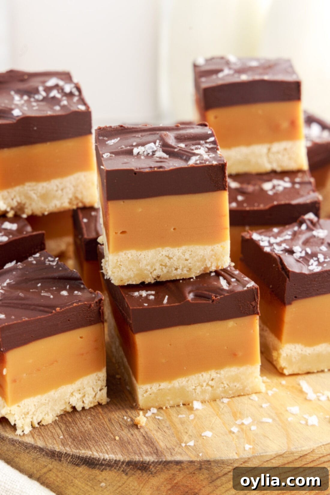Millionaires Bars 3 Stacks of Millionaire’s Bars neatly arranged on a rustic wooden board, highlighting their golden, caramel, and chocolate layers.