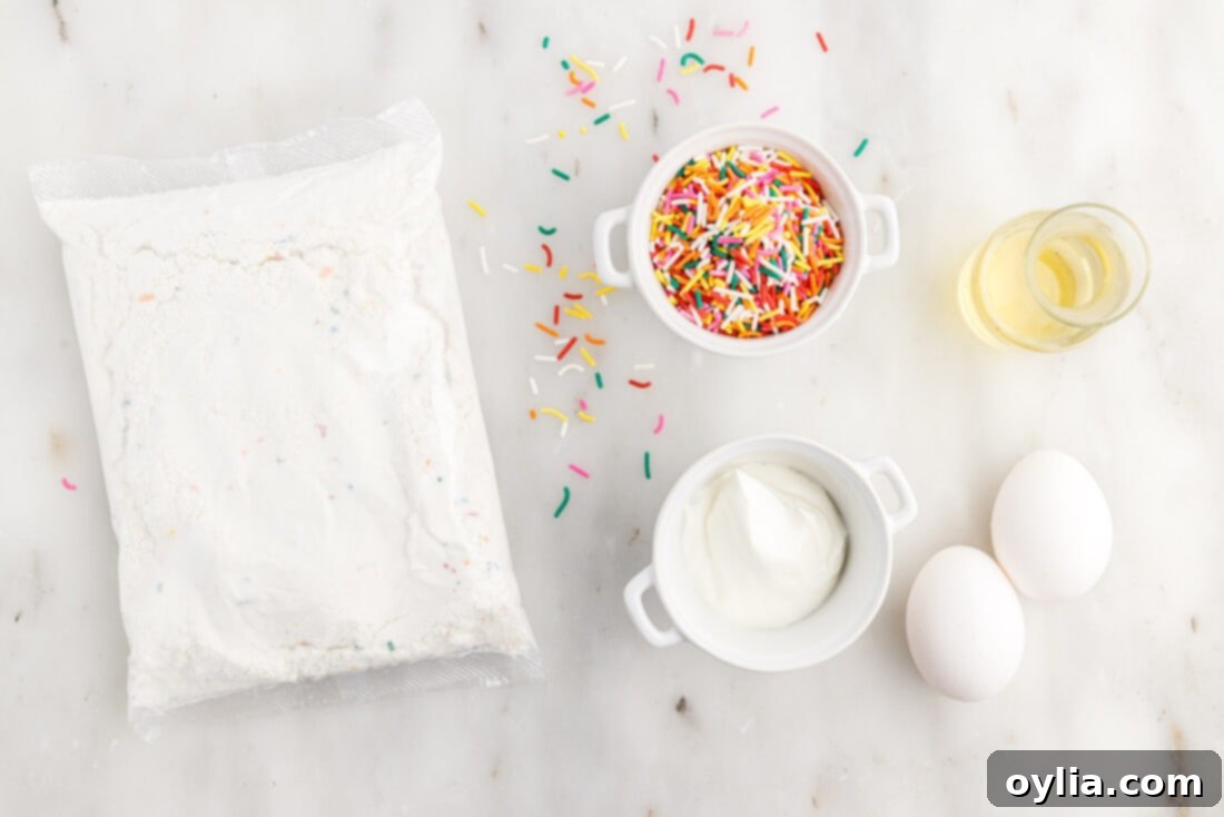 Confetti Cake Cookie Bliss 4 All ingredients for Funfetti Cake Mix Cookies laid out on a surface, including a box of cake mix, eggs, oil, sour cream, and sprinkles.