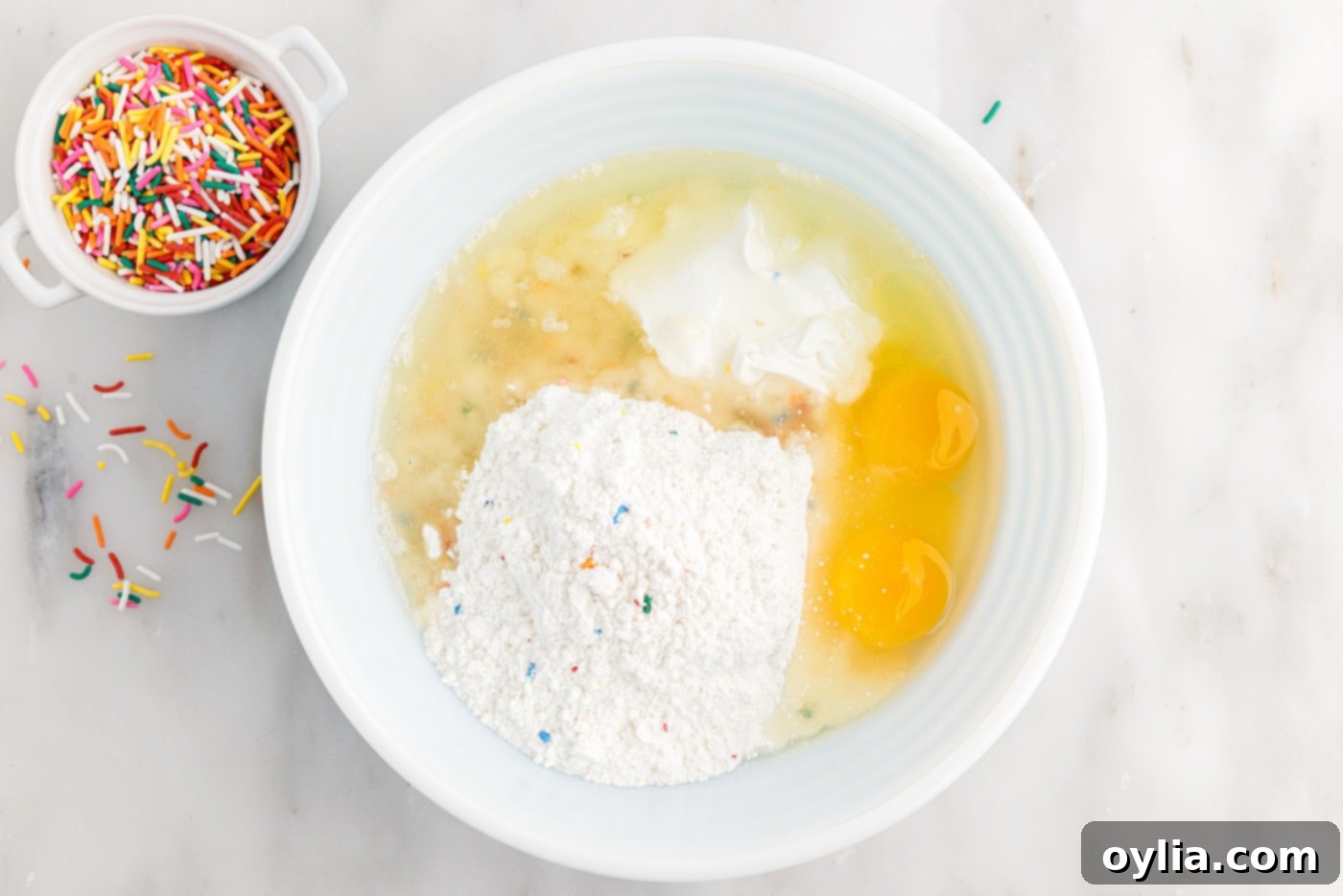 Cake mix, eggs, sour cream, and oil in a mixing bowl being stirred together to form the cookie dough.