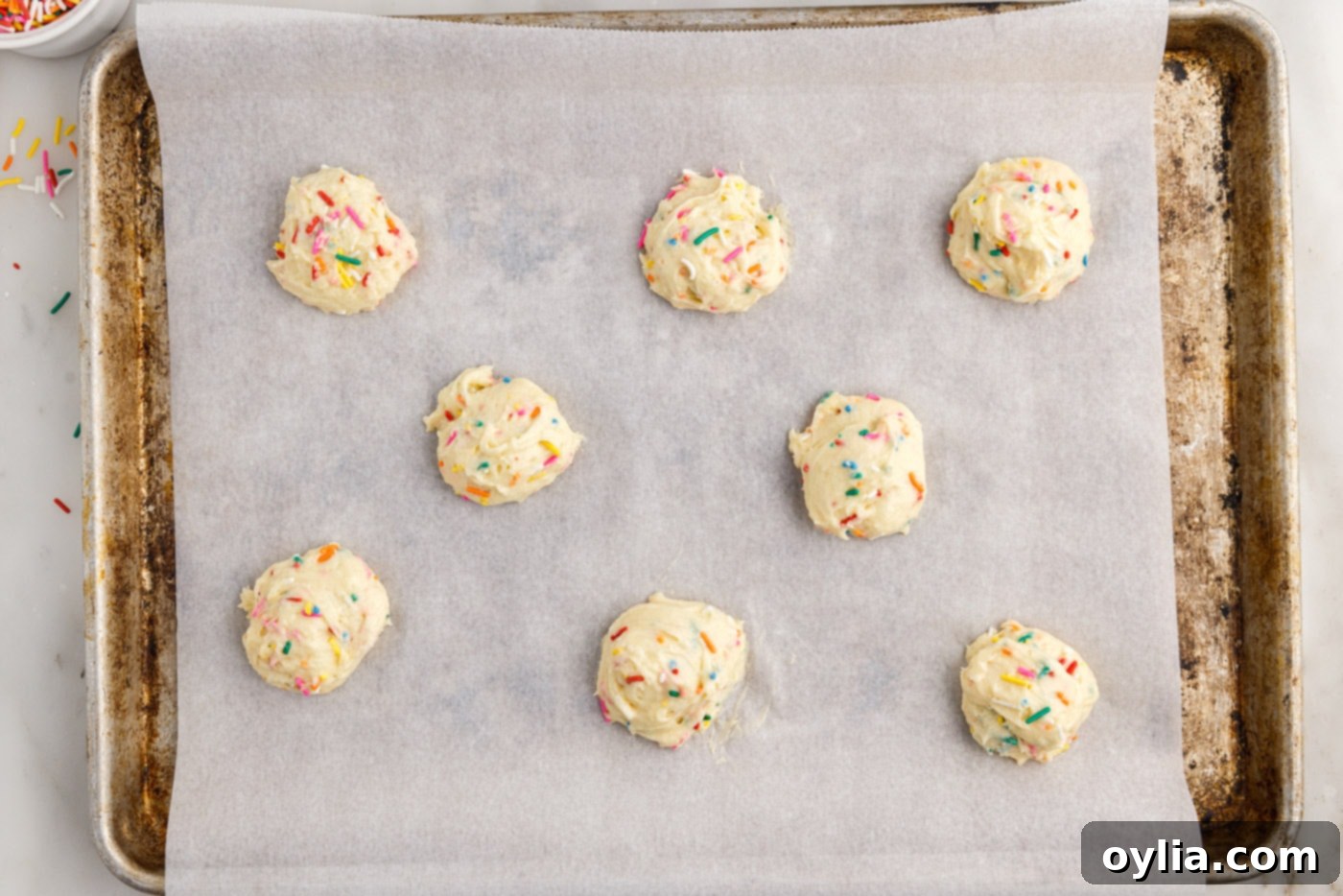Neatly scooped funfetti cookie dough balls arranged on a parchment-lined baking sheet, ready for the oven.