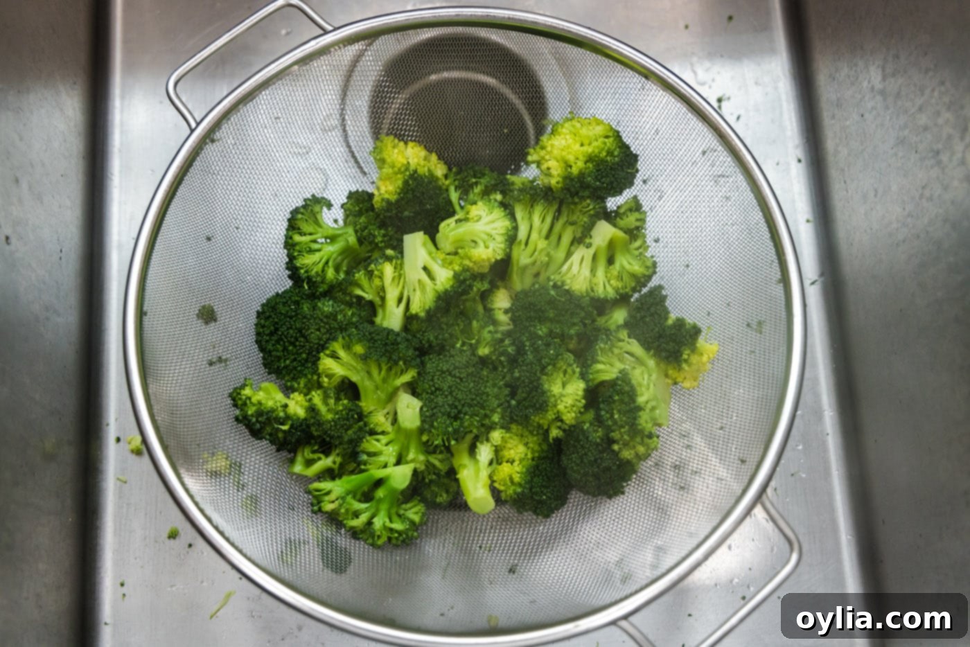 Cooked broccoli florets in a colander, draining excess water.