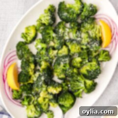 Instant Pot Broccoli on a white platter with onions and lemon wedges, showcasing a fresh and appealing presentation.