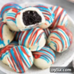 Red White and Blue Oreo Truffle with a bite taken out resting on top of a bunch of Red White and Blue Oreo Truffles in a bowl