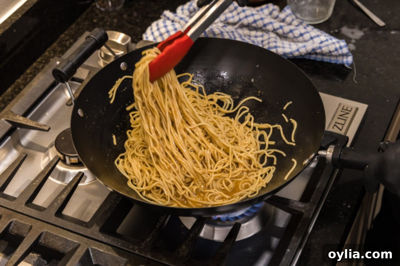 tongs picking up thickened teriyaki noodles in a wok, showing the finished texture