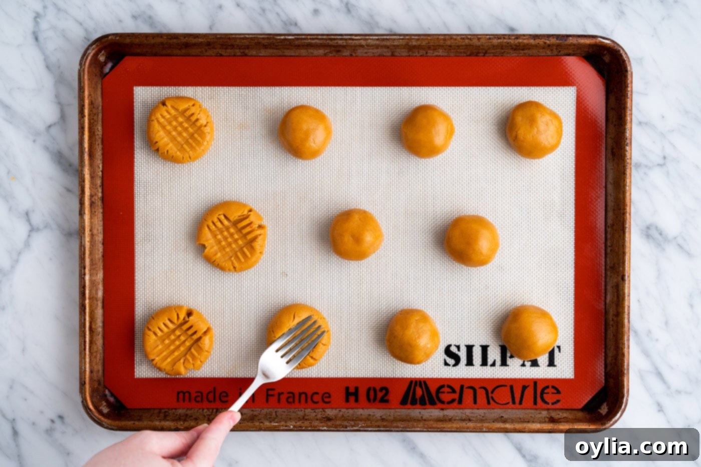 A fork pressing down on a peanut butter cookie dough ball to create the classic cross-hatch pattern.