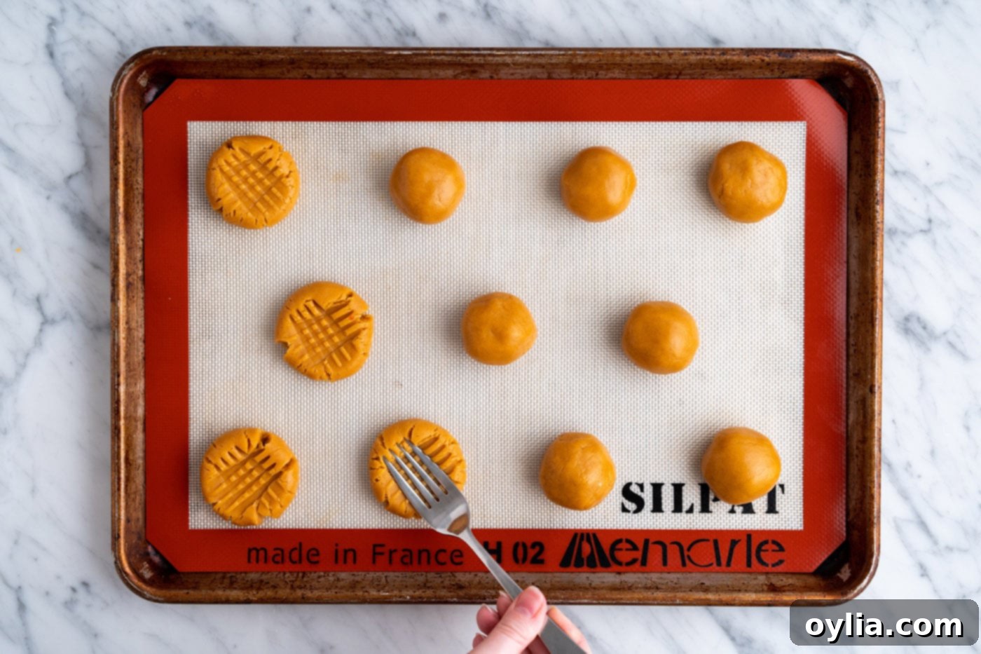 Multiple cookie dough balls on a baking sheet, each with the distinctive cross-hatch pattern made by a fork.