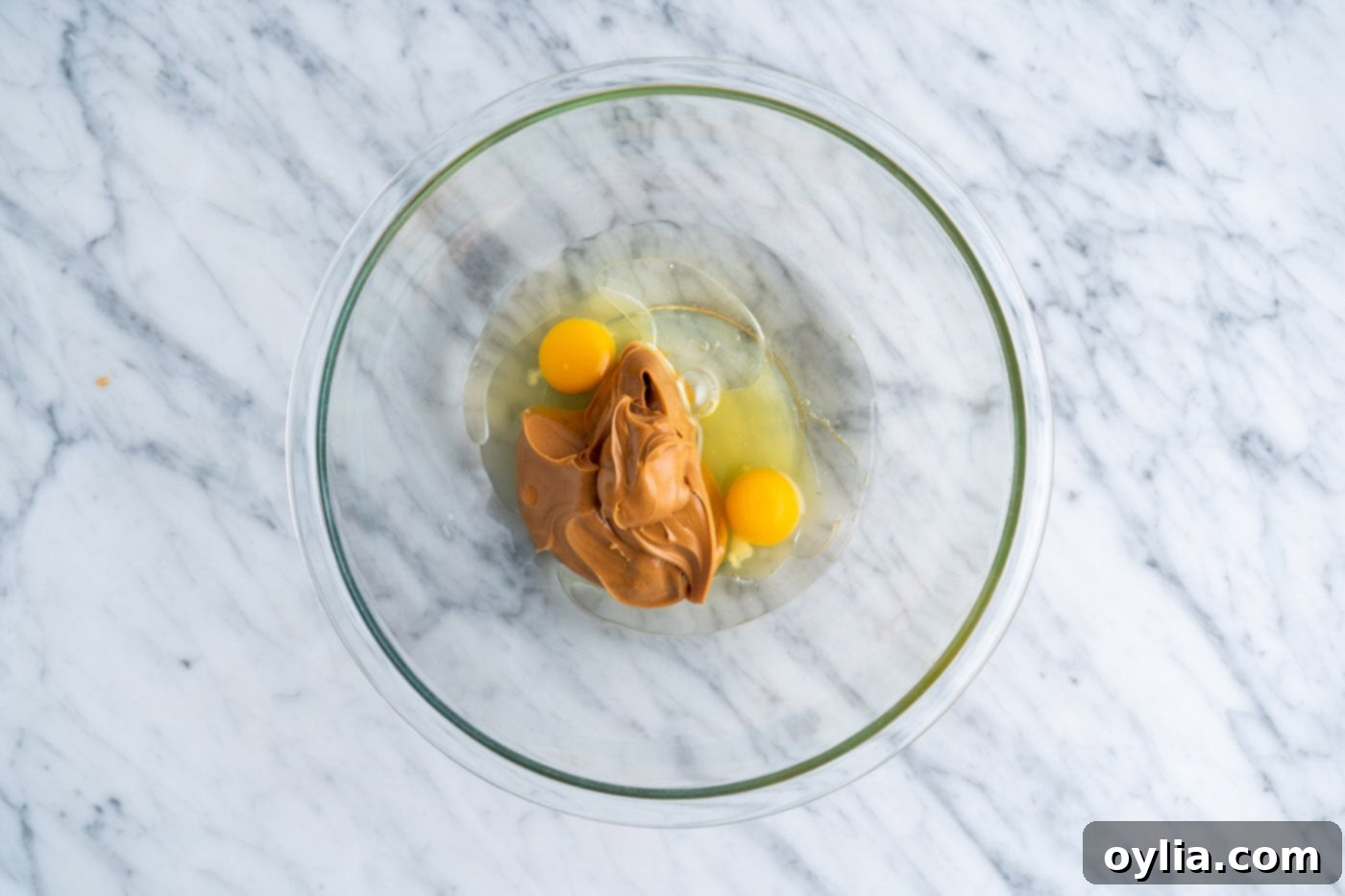 A bowl containing eggs, creamy peanut butter, and vegetable oil before mixing.