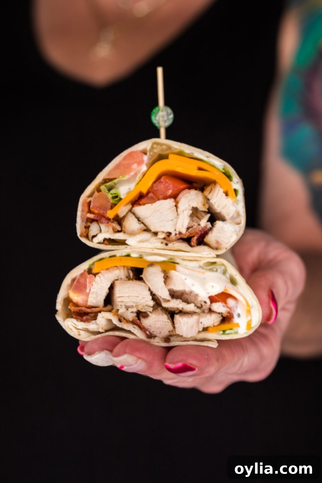 Hand holding two halves of a Chicken Bacon Ranch Wrap stacked on top of each other
