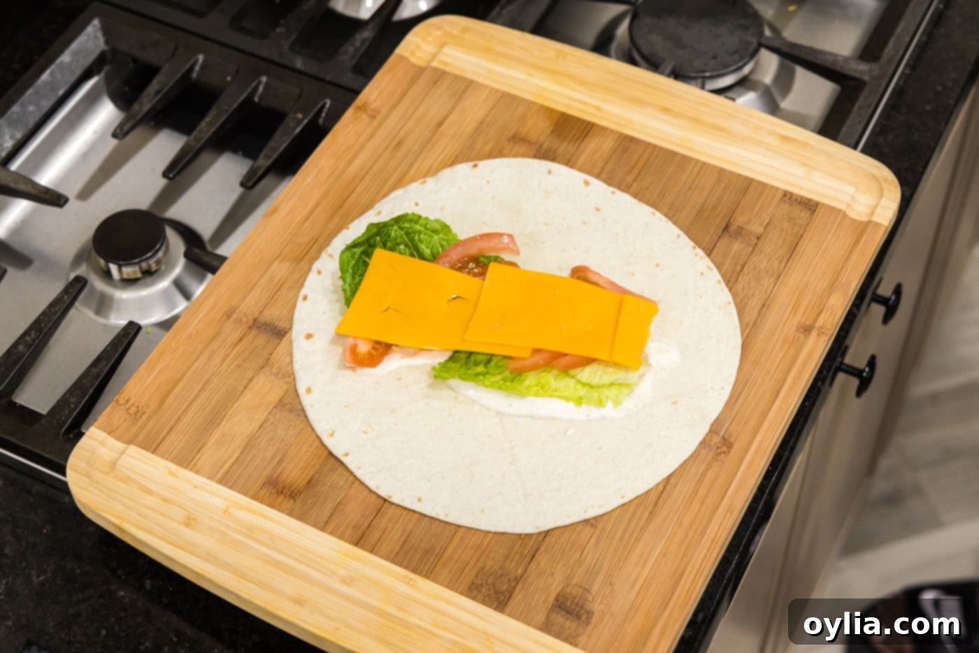 sliced cheese on top of lettuce, ranch, and tomato tortilla