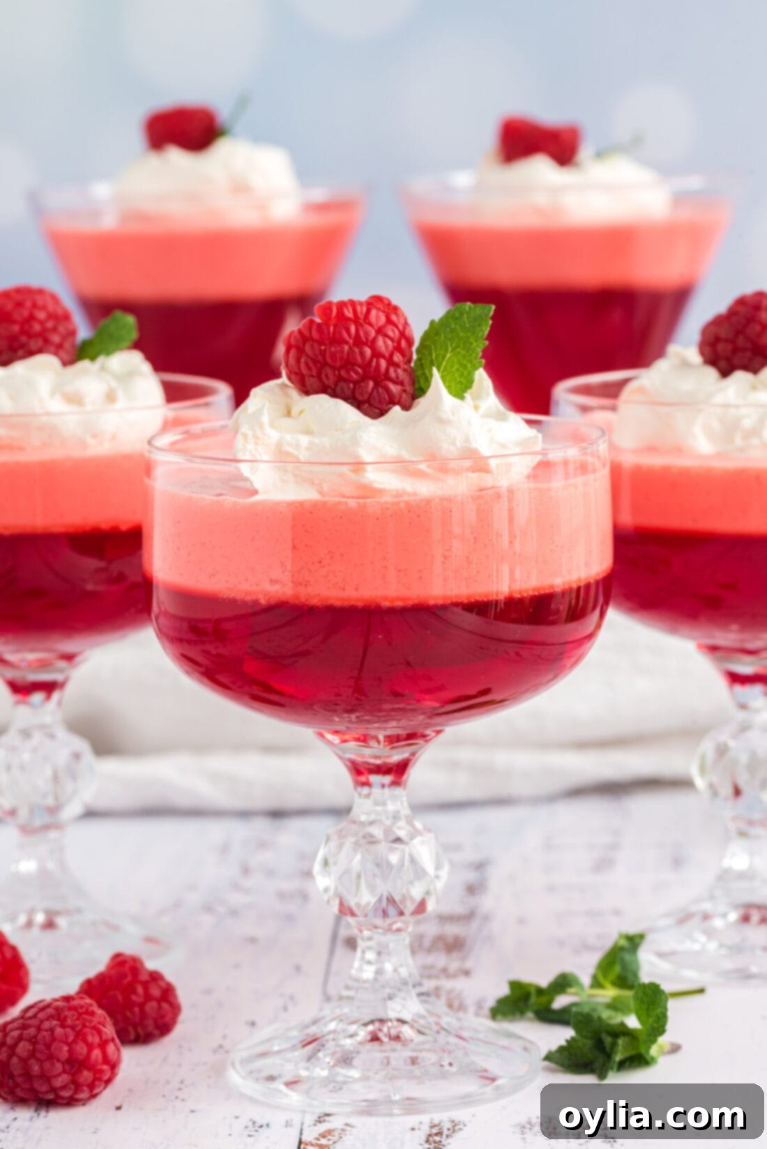 Raspberry Jell-O Parfaits with whipped cream and fresh raspberries, showcasing beautiful layers in a glass dessert dish.