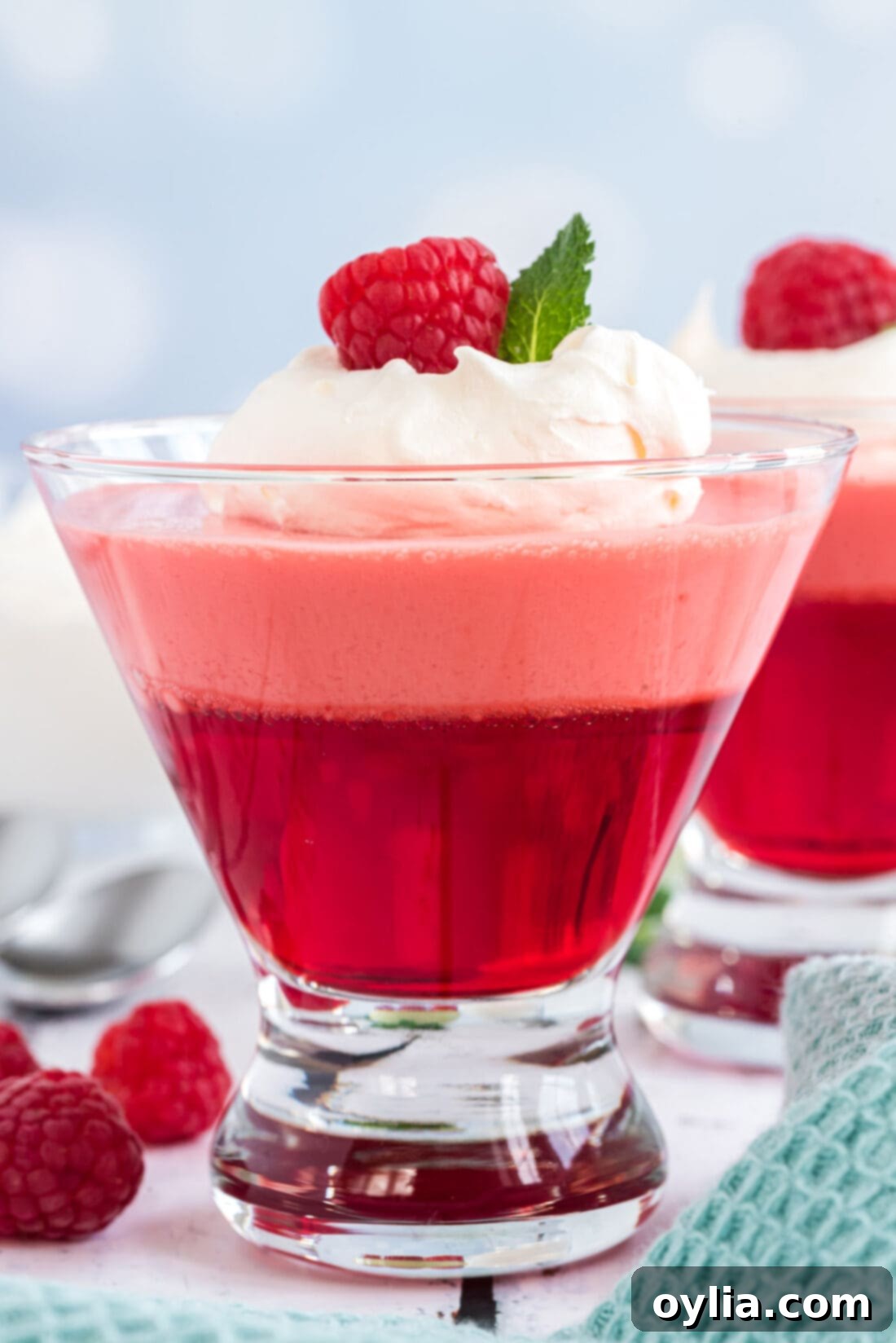 A single, perfectly layered Raspberry Jell-O Parfait served in an elegant glass dessert dish, garnished with whipped cream.