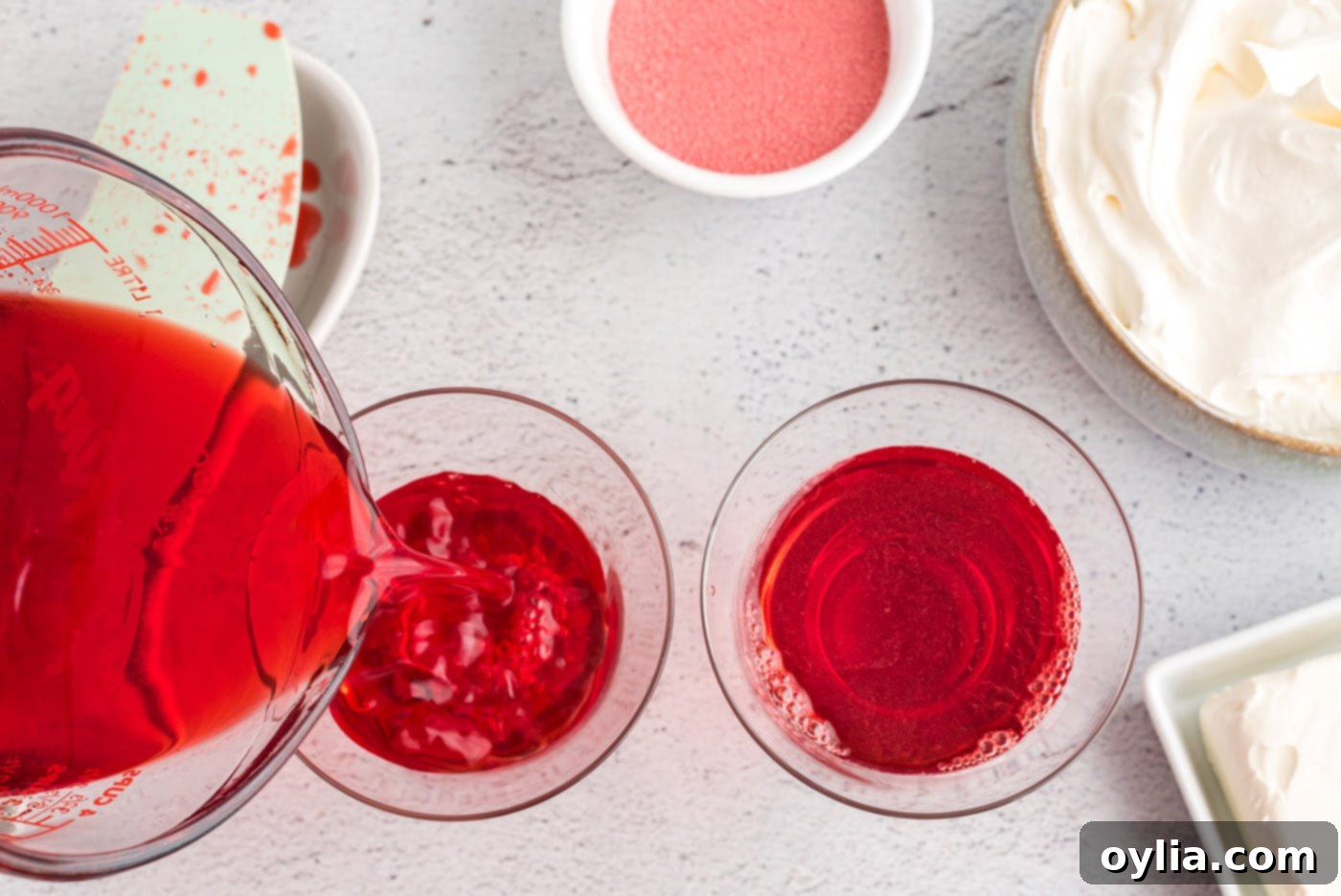 Carefully pouring the vibrant red liquid Jell-O mixture into individual clear trifle dessert dishes to form the solid bottom layer.