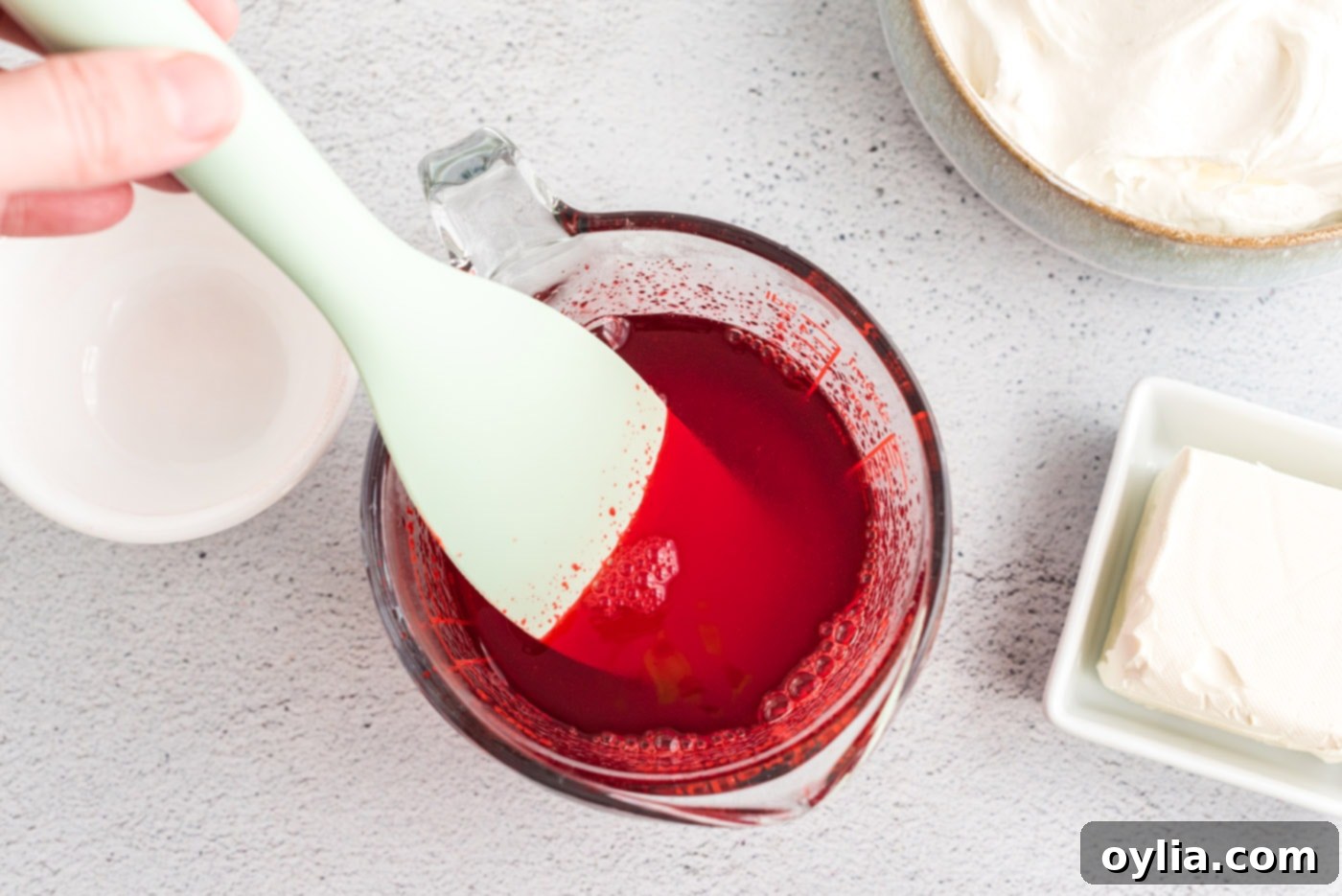 Mixing the second batch of Jell-O powder with hot water in a bowl for the creamy layer, ensuring it dissolves completely.