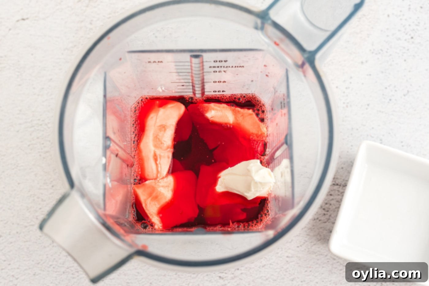 Softened cream cheese and the dissolved Jell-O mixture being blended together in a food processor to create a smooth base for the creamy layer.