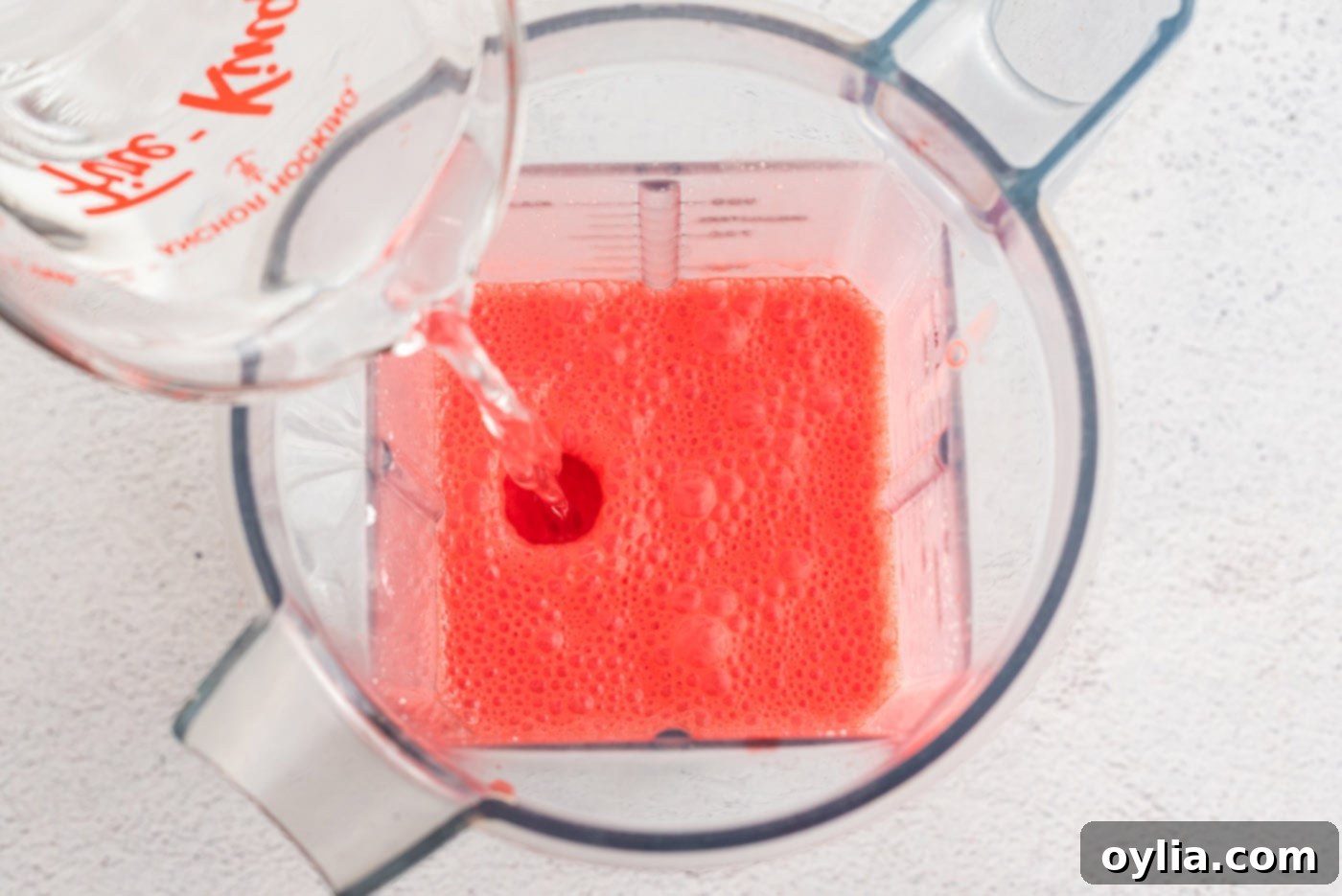 Adding cold water to the Jell-O and cream cheese mixture in a blender, followed by blending until smooth.