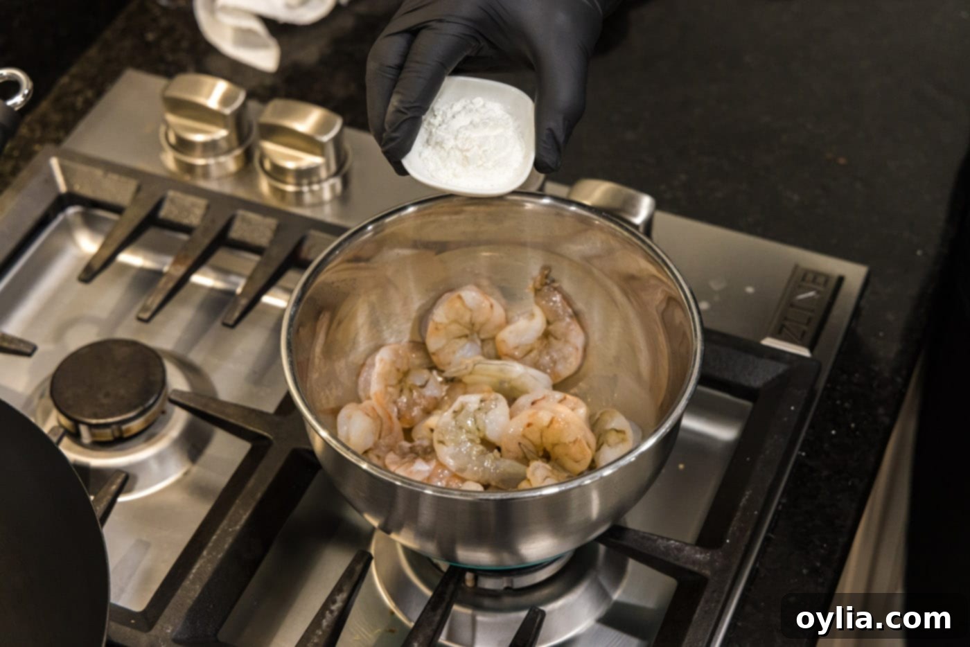 Raw shrimp being tossed with cornstarch in a large mixing bowl.