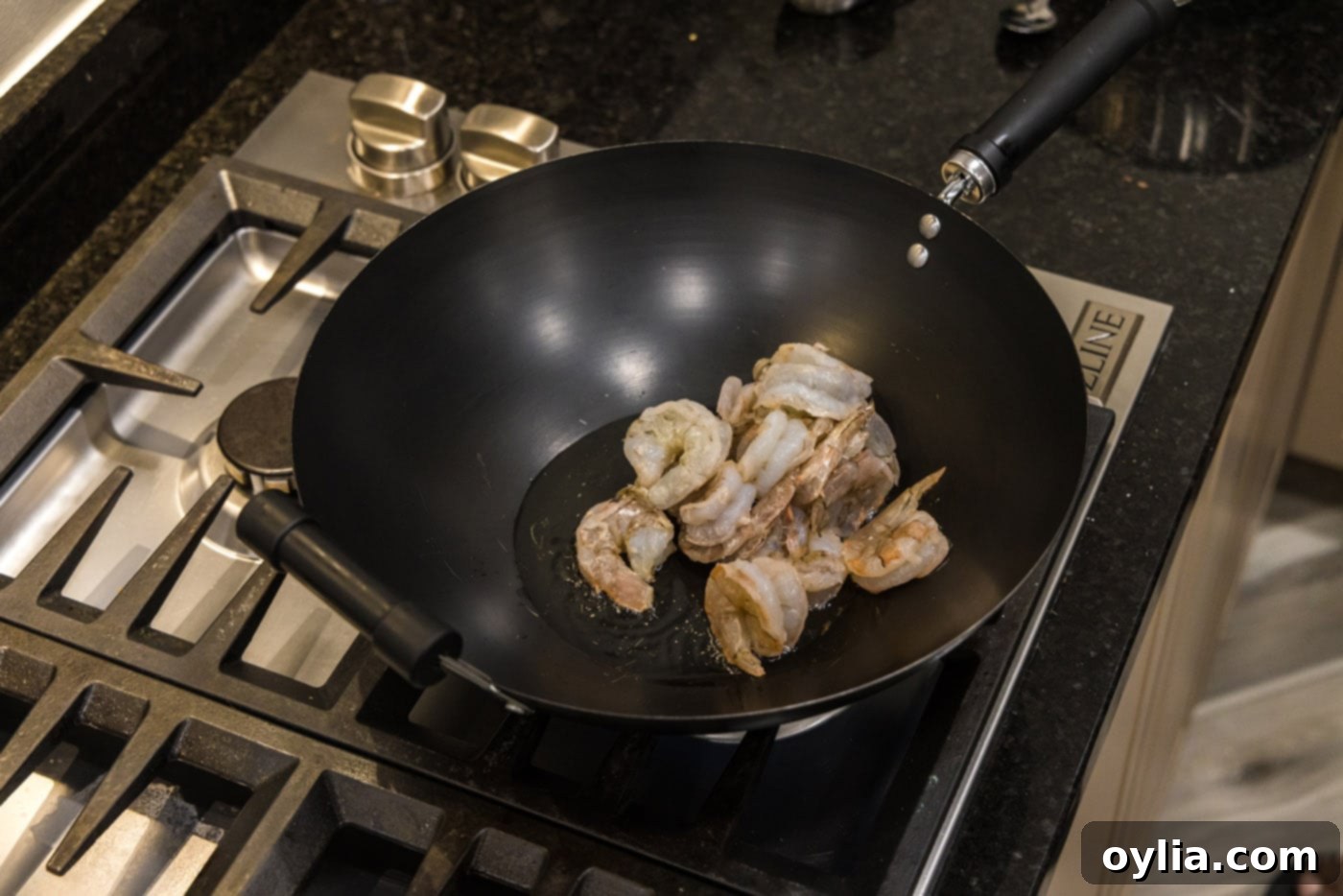 Shrimp cooking in olive oil in a hot wok, beginning to turn pink and opaque.