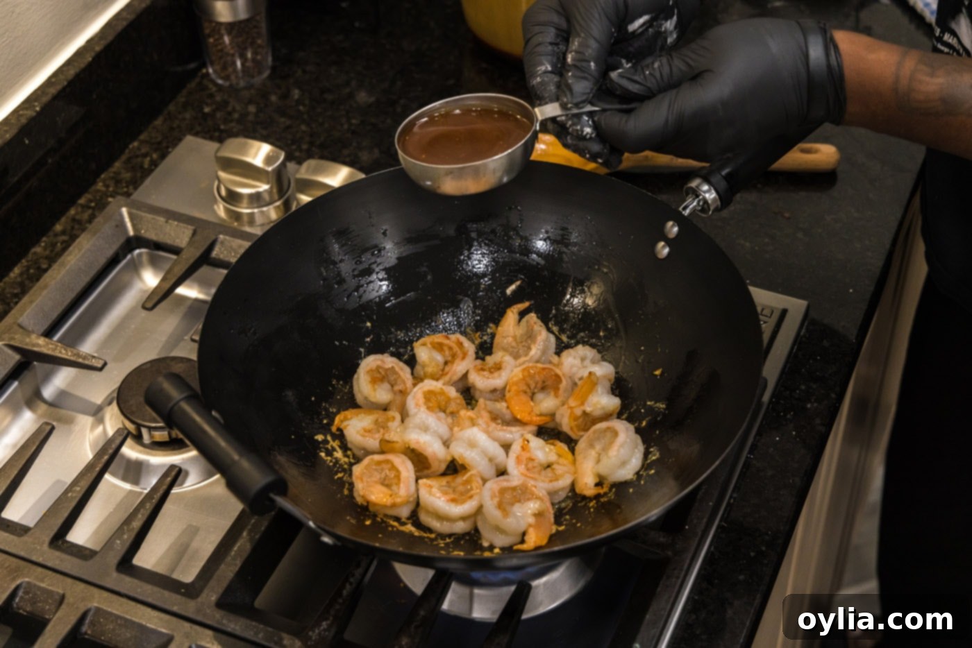 Homemade teriyaki sauce being poured over stir-fried shrimp in a wok.