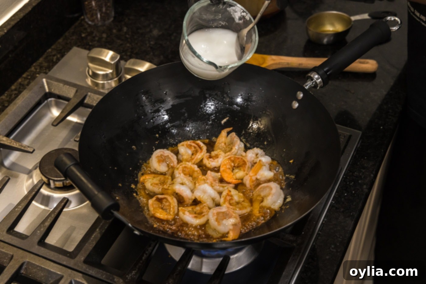 A cornstarch slurry being poured into the teriyaki shrimp mixture in a wok to thicken the sauce.