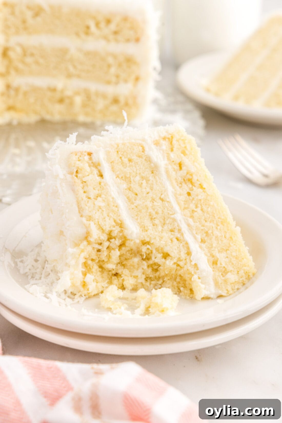 Coconut Cake 2 A delectable slice of coconut cake, featuring moist layers, creamy frosting, and shredded coconut, with a bite playfully removed.