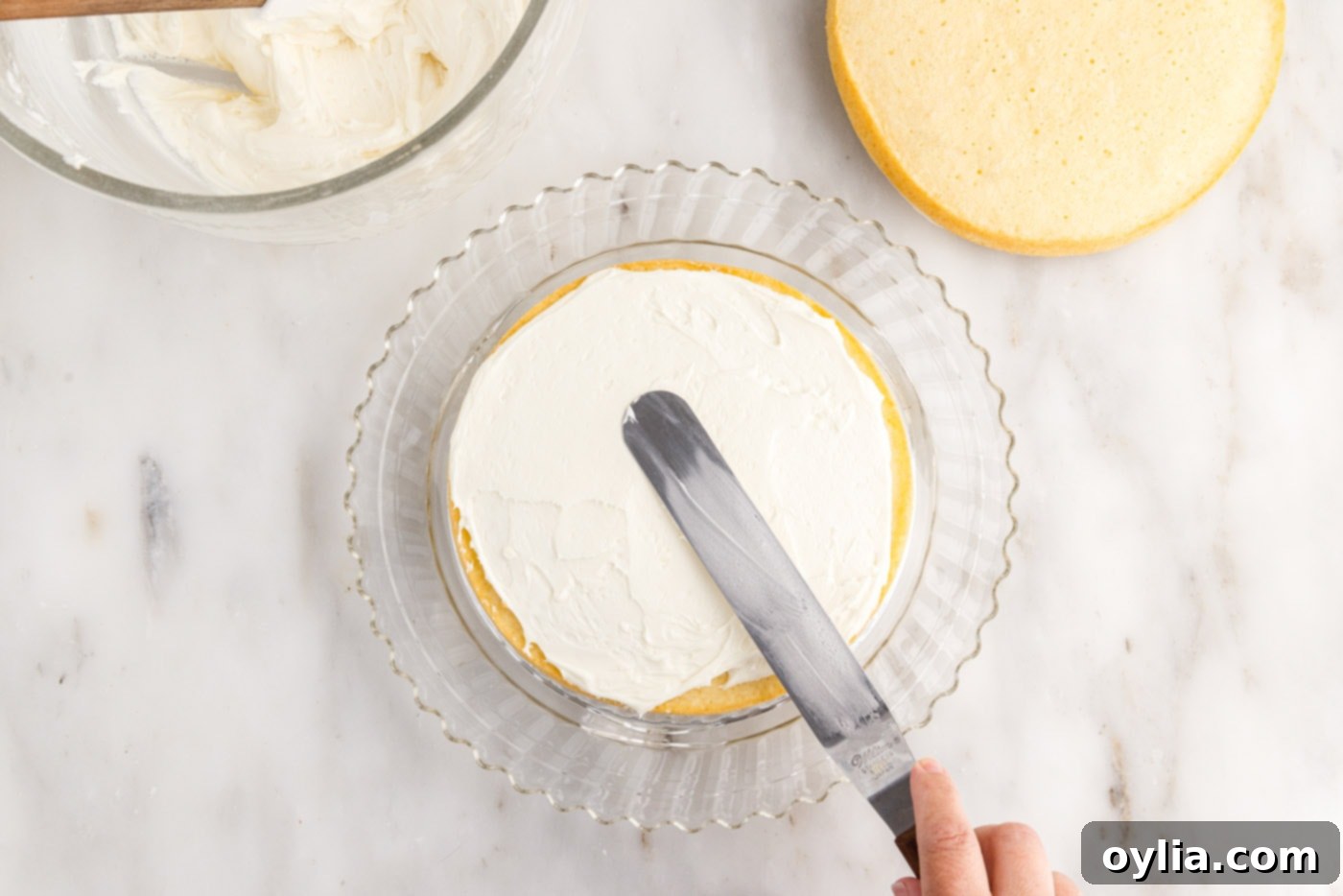 A smooth layer of cream cheese frosting is spread evenly over the top of the first cake layer, preparing it for the next tier.