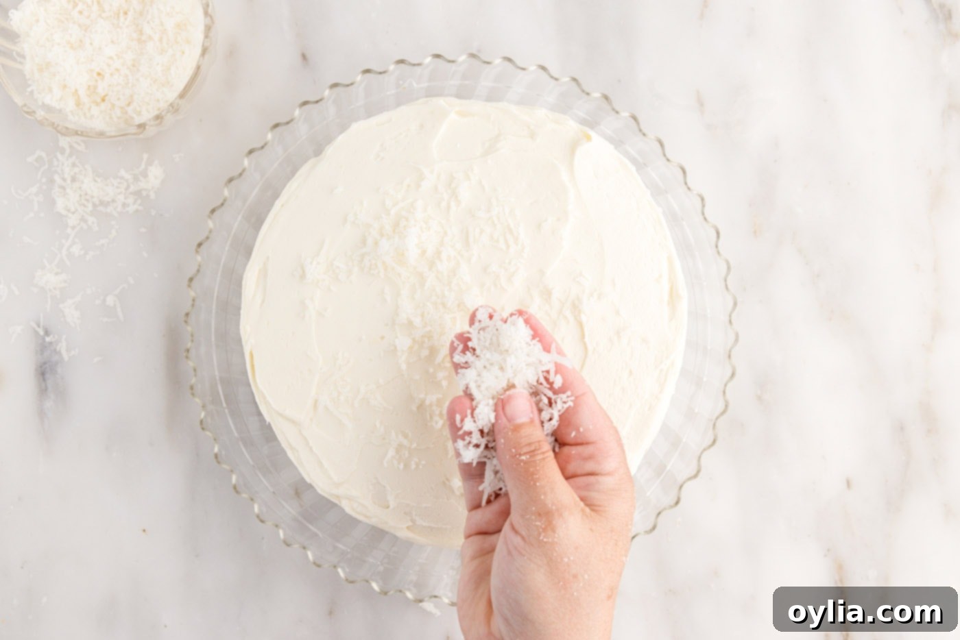 Sweetened shredded coconut is sprinkled generously over the top of the frosted coconut cake, adding texture and flavor to the final presentation.