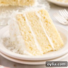 Coconut Cake 21 A pristine slice of fluffy coconut cake, beautifully layered with cream cheese frosting and garnished with shredded coconut, resting on a small white plate.