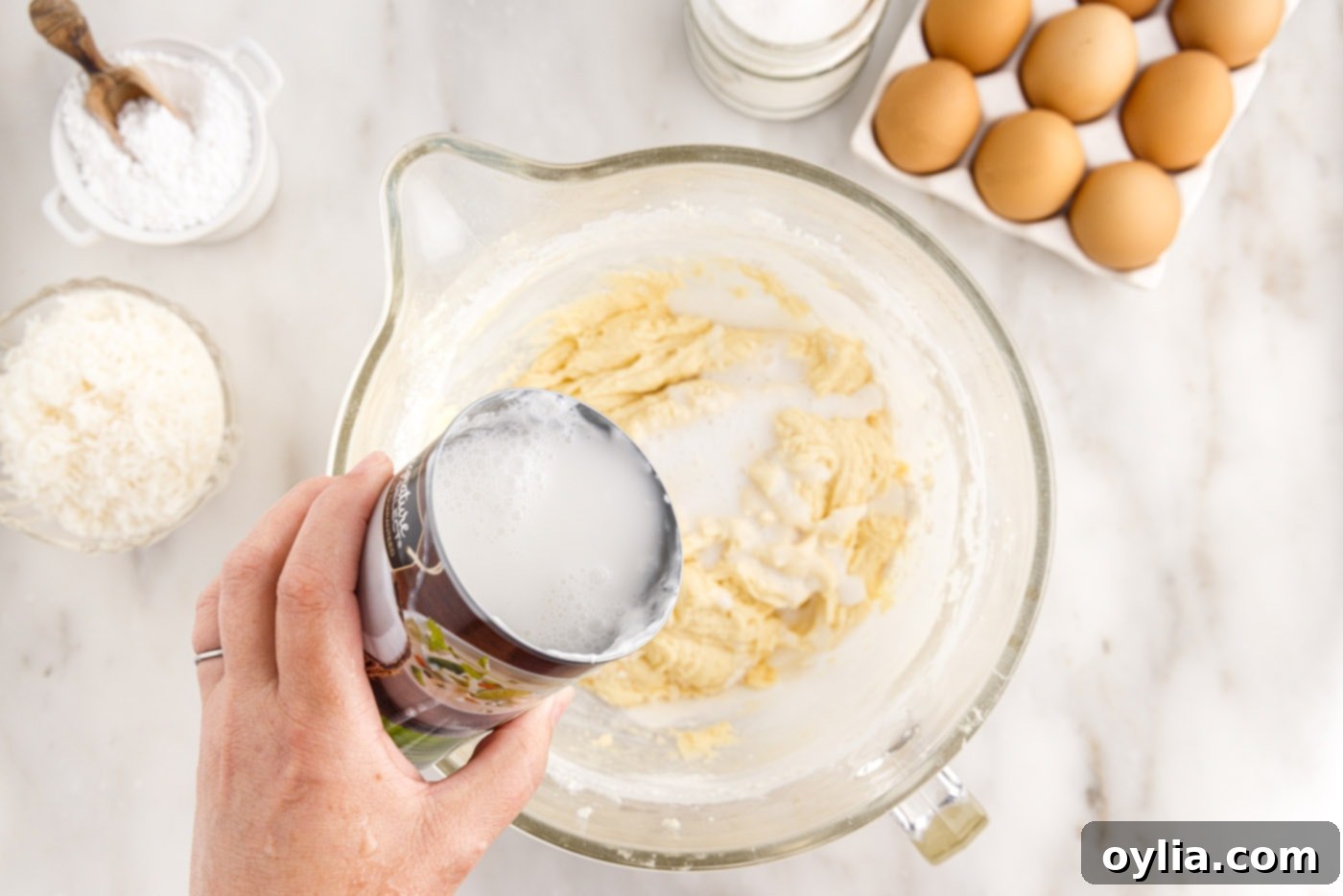 Unsweetened coconut milk is being poured into the cake batter, alternating with dry ingredients for a perfectly blended consistency.