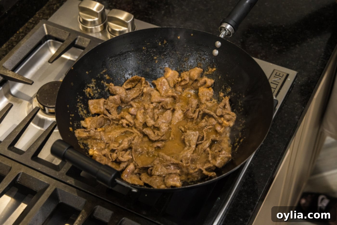 Thinly sliced beef strips being added to a hot wok with olive oil.