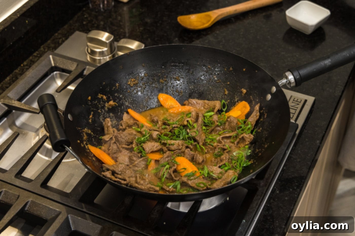 Beef bulgogi cooking in a wok with sliced carrots and green onions added, nearing completion.