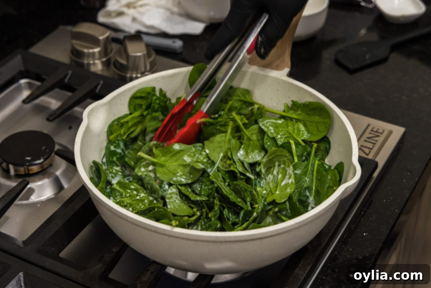 Decadent Creamed Spinach 9 tongs tossing spinach in skillet