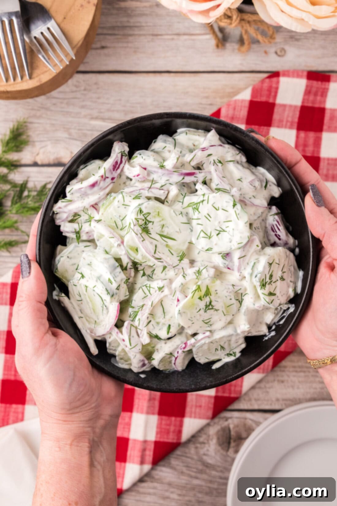 Hands holding a bowl of Creamy Cucumber Salad