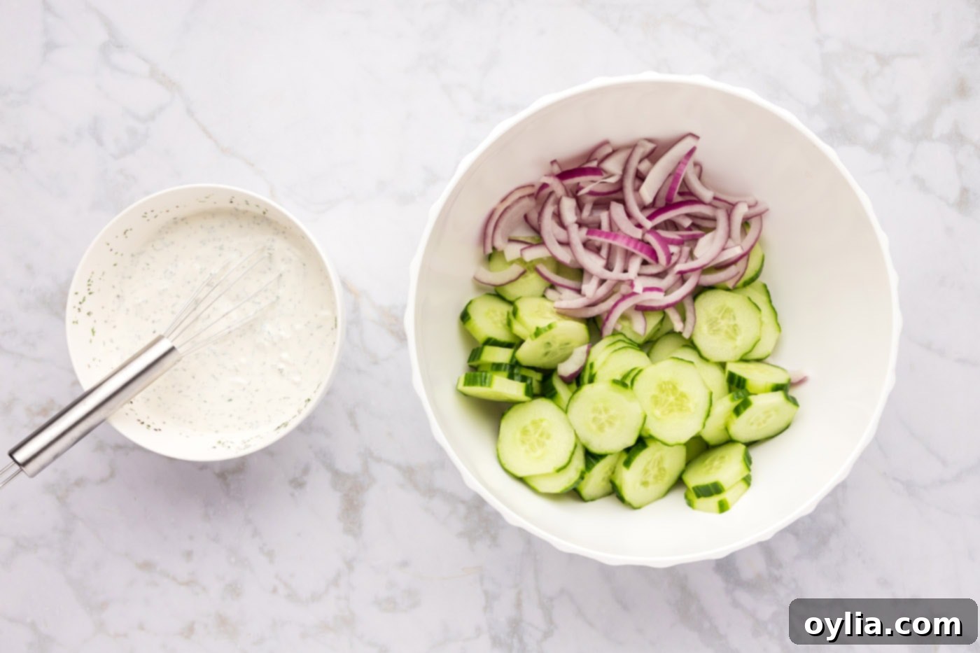 red onion and cucumber in a mixing bowl along with creamy dressing on the side