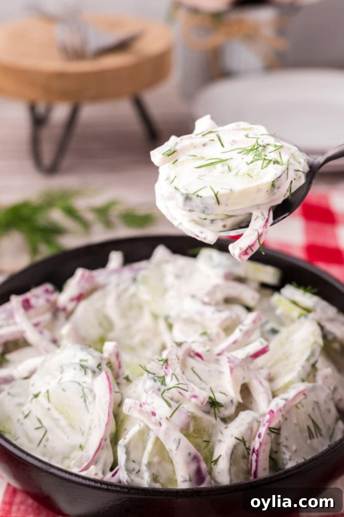 Spoonful of Creamy Cucumber Salad held above a bowl of Creamy Cucumber Salad