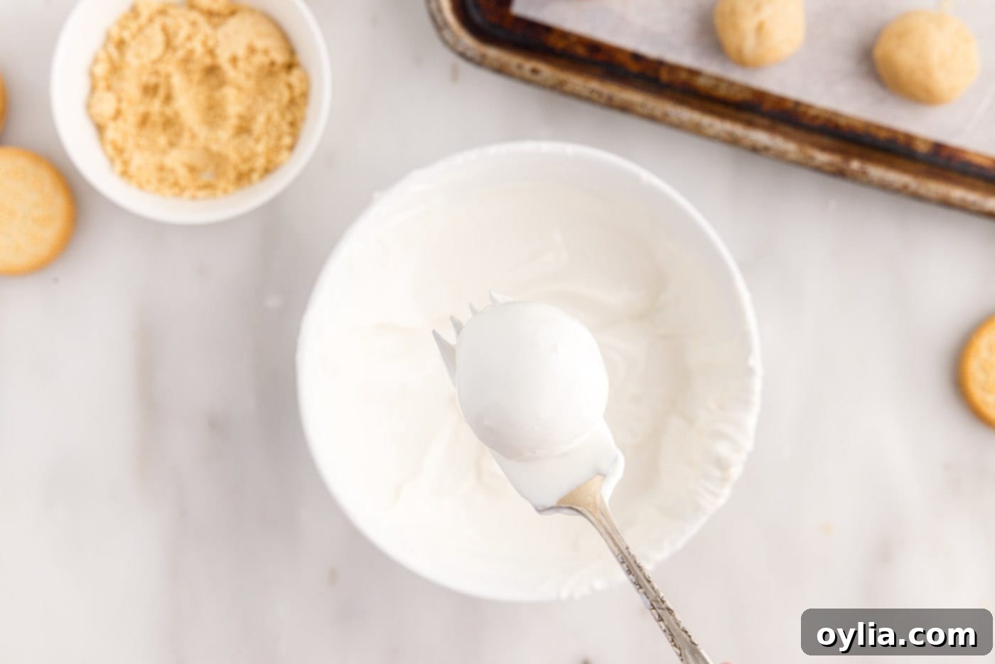 Dipping a Golden Oreo truffle into melted white chocolate coating using a fork