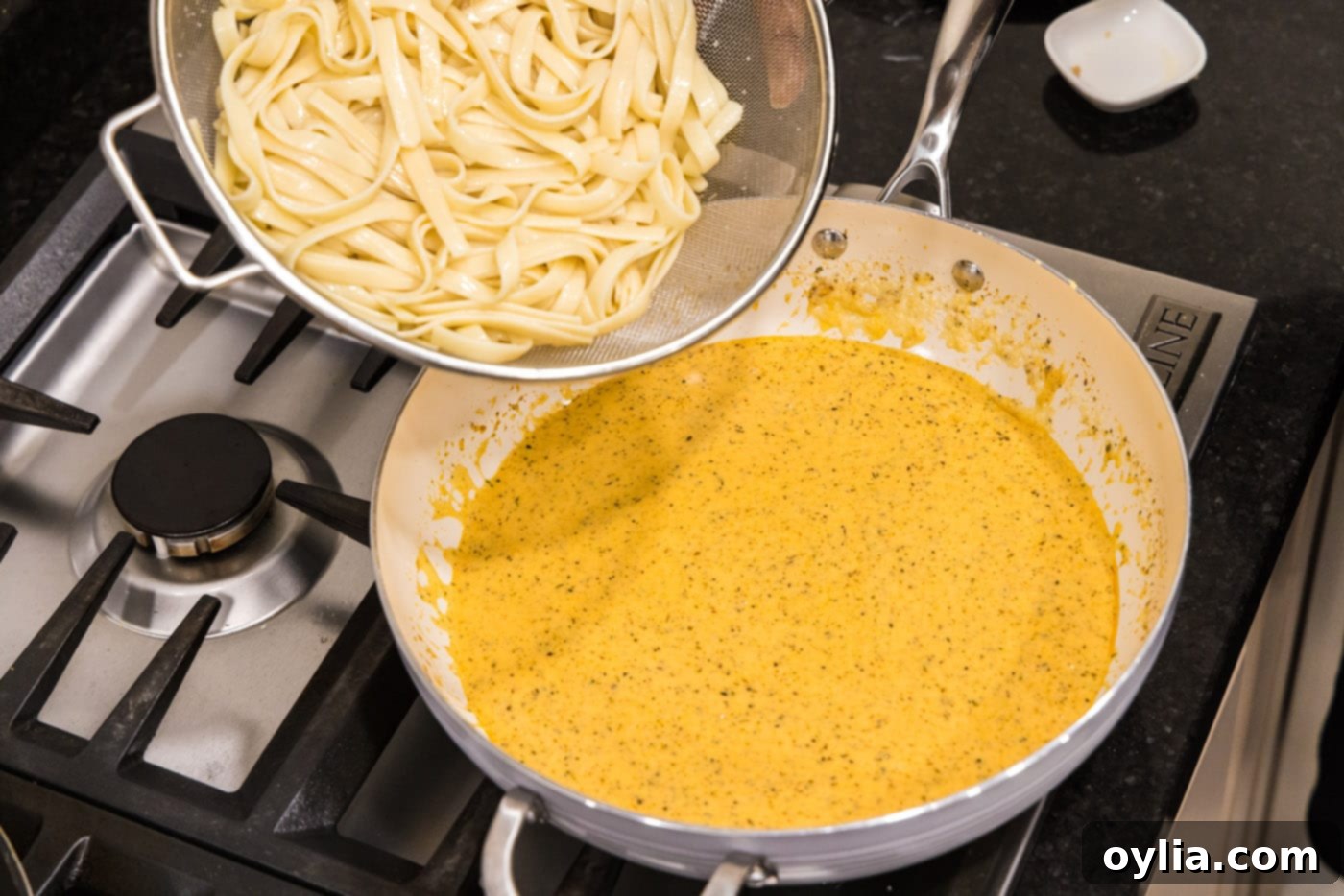 Cooked fettuccine noodles being added to the alfredo sauce in a skillet, ready to be tossed