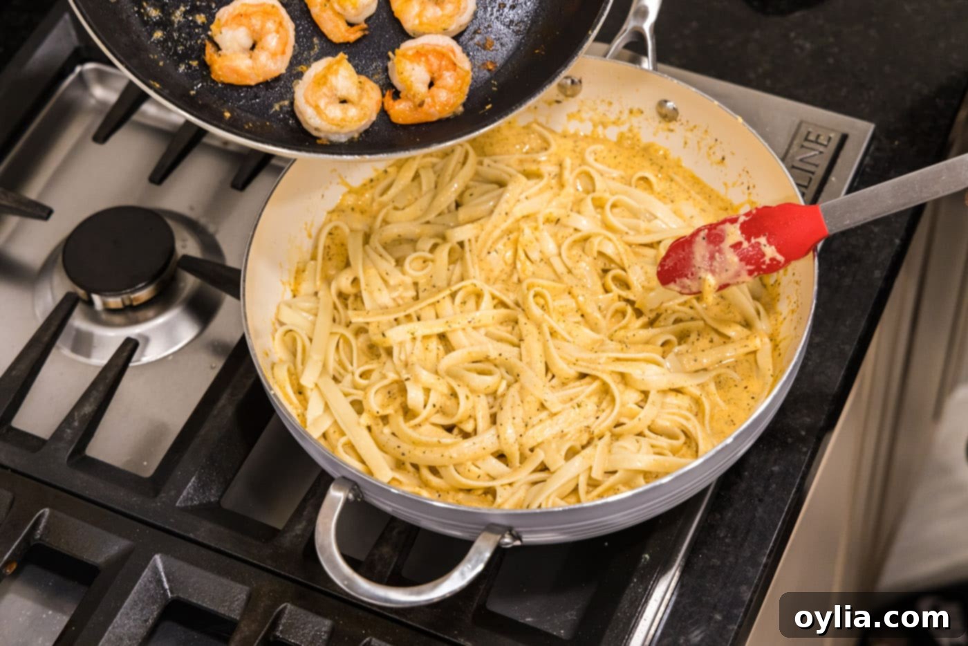 Sautéed shrimp being added to the fettuccine and alfredo sauce mixture in the skillet