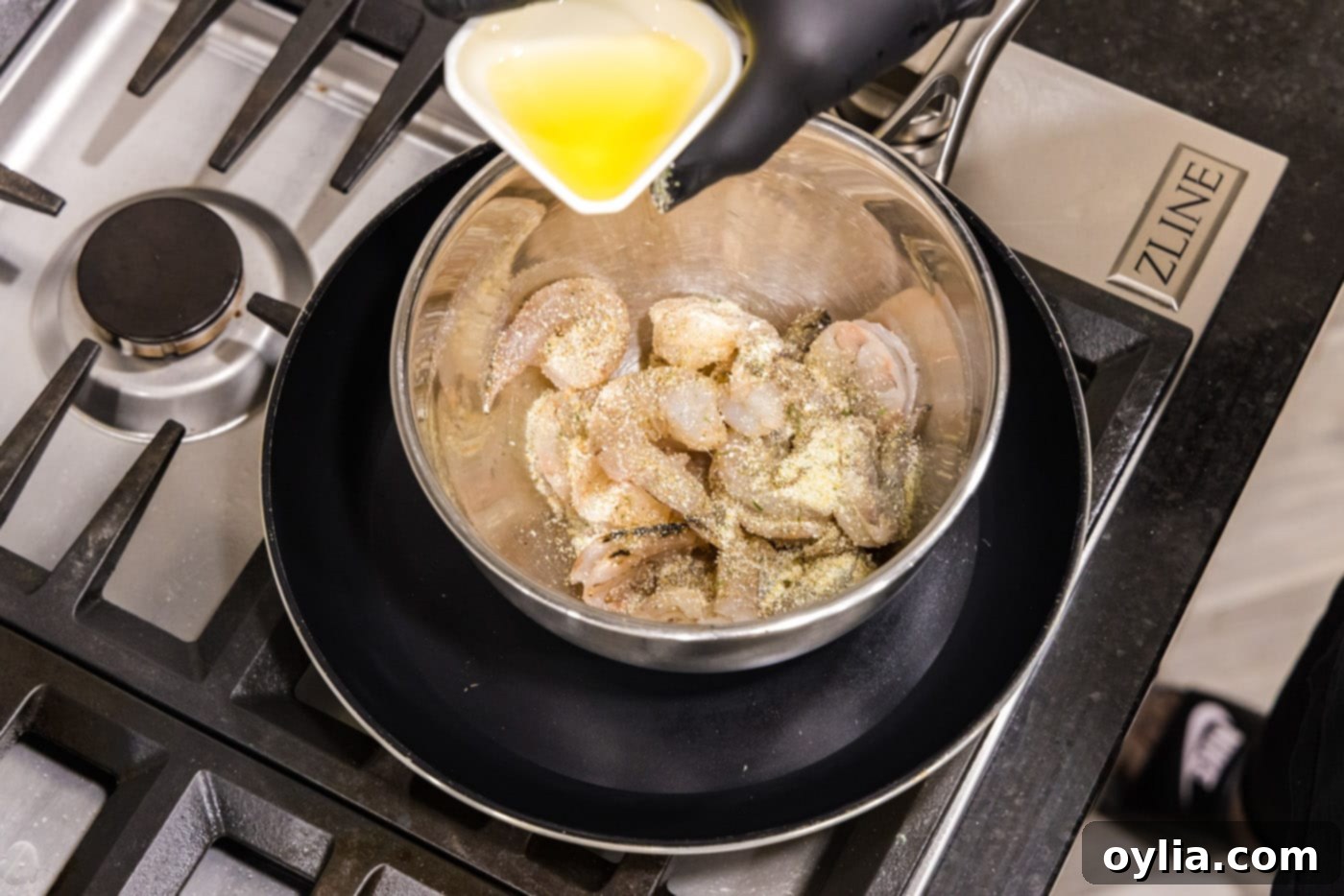 Raw shrimp being tossed with olive oil and garlic salt in a medium bowl