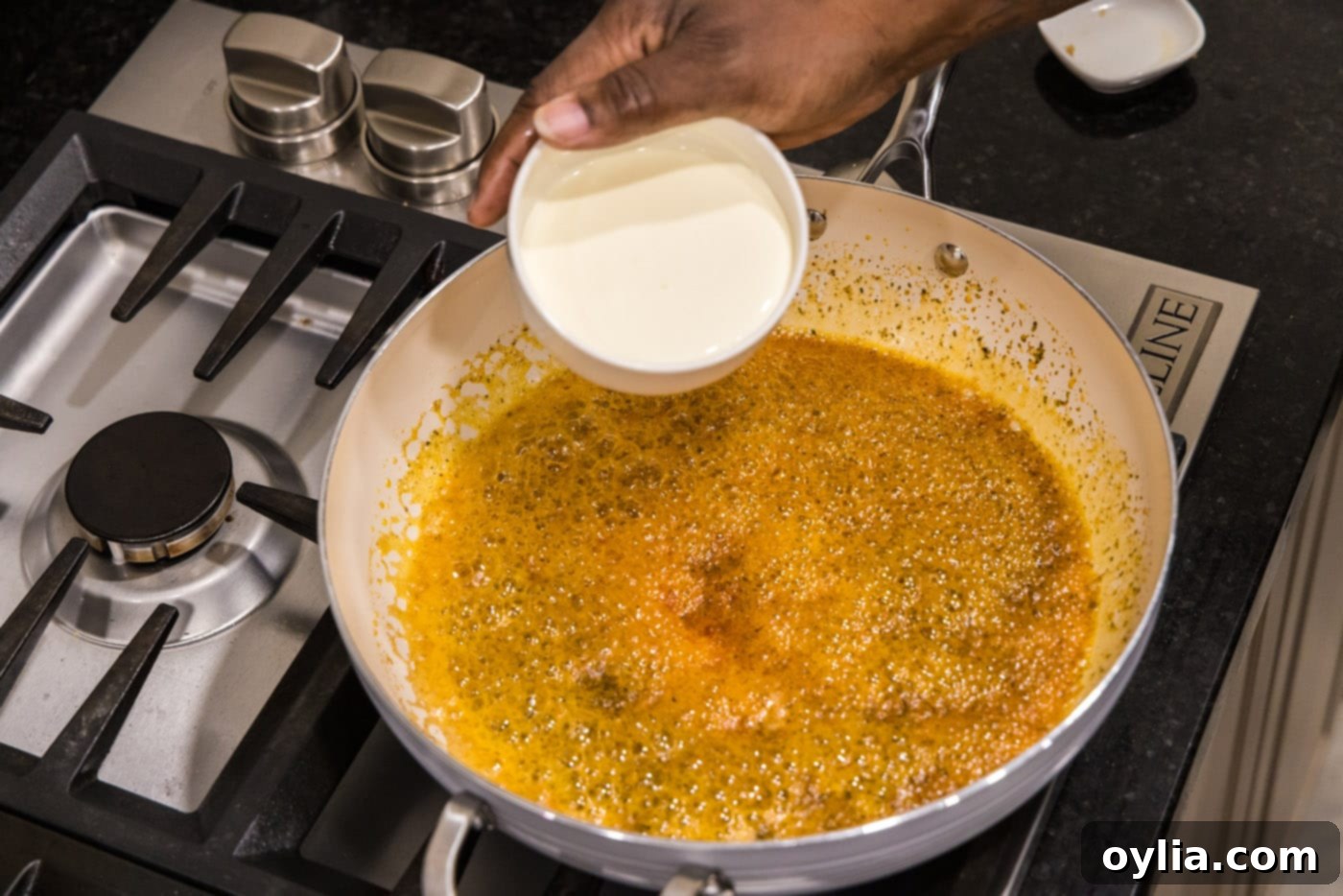 Heavy cream being poured into the skillet to form the base of the alfredo sauce