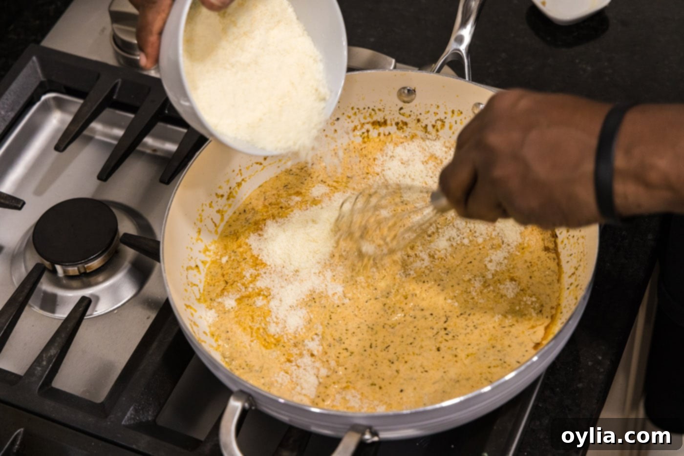 Parmesan cheese being sprinkled into the simmering cream sauce, ready to be whisked until smooth