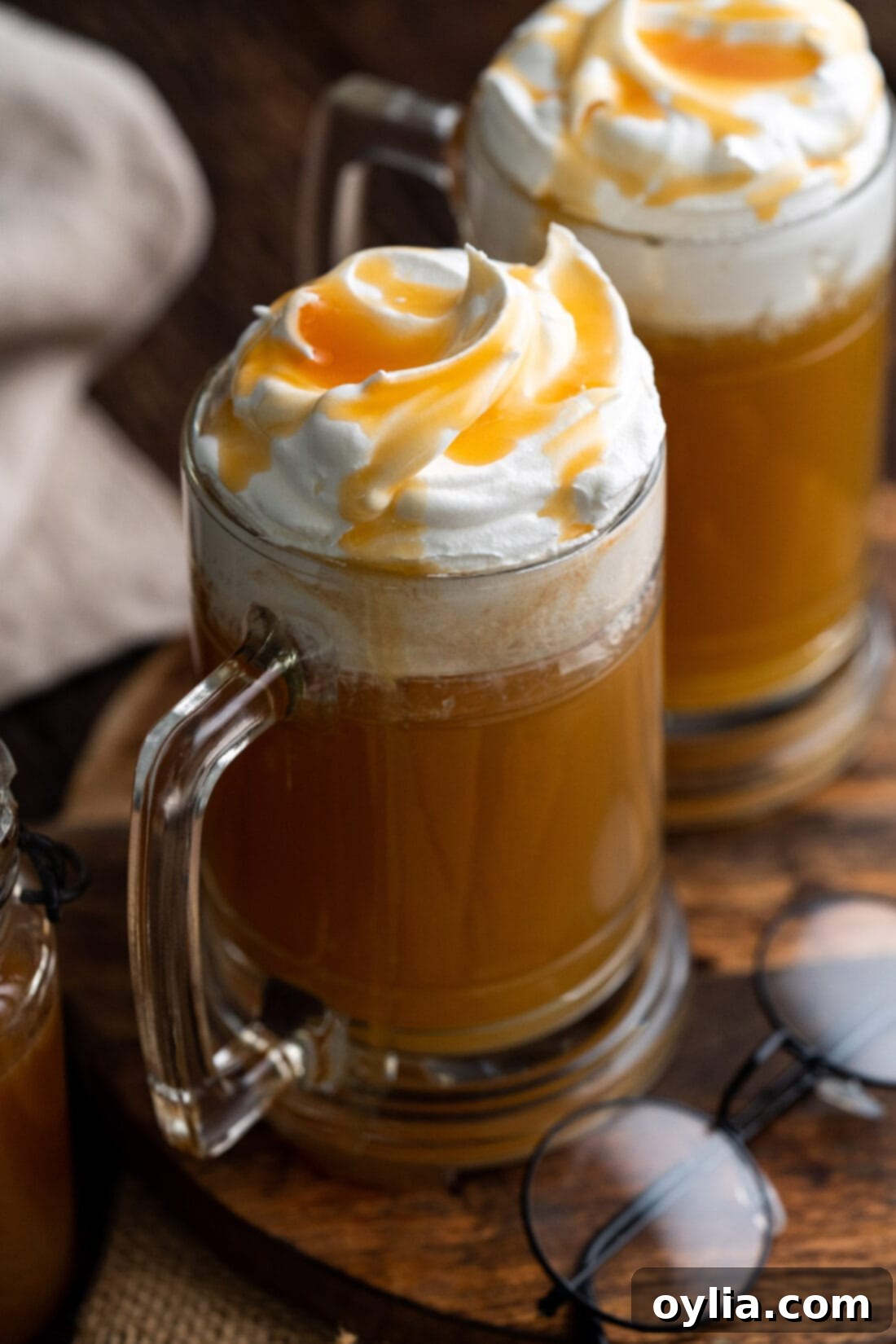 Two glasses of Butterbeer topped with a generous layer of whipped cream and a drizzle of butterscotch syrup, ready to be enjoyed.