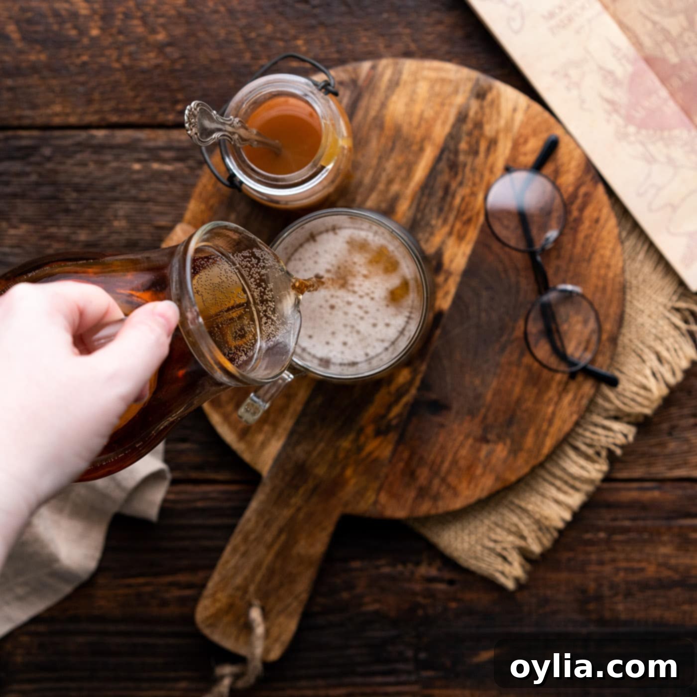 A hand pouring cream soda into a large glass mug, beginning the Butterbeer preparation.