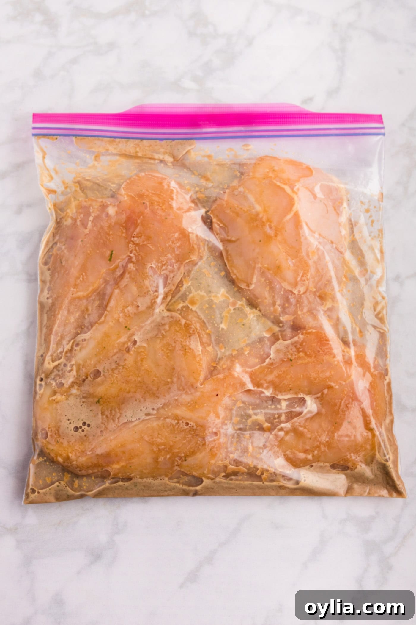 Raw chicken breasts fully submerged in the honey garlic marinade inside a sealed zip-top bag.