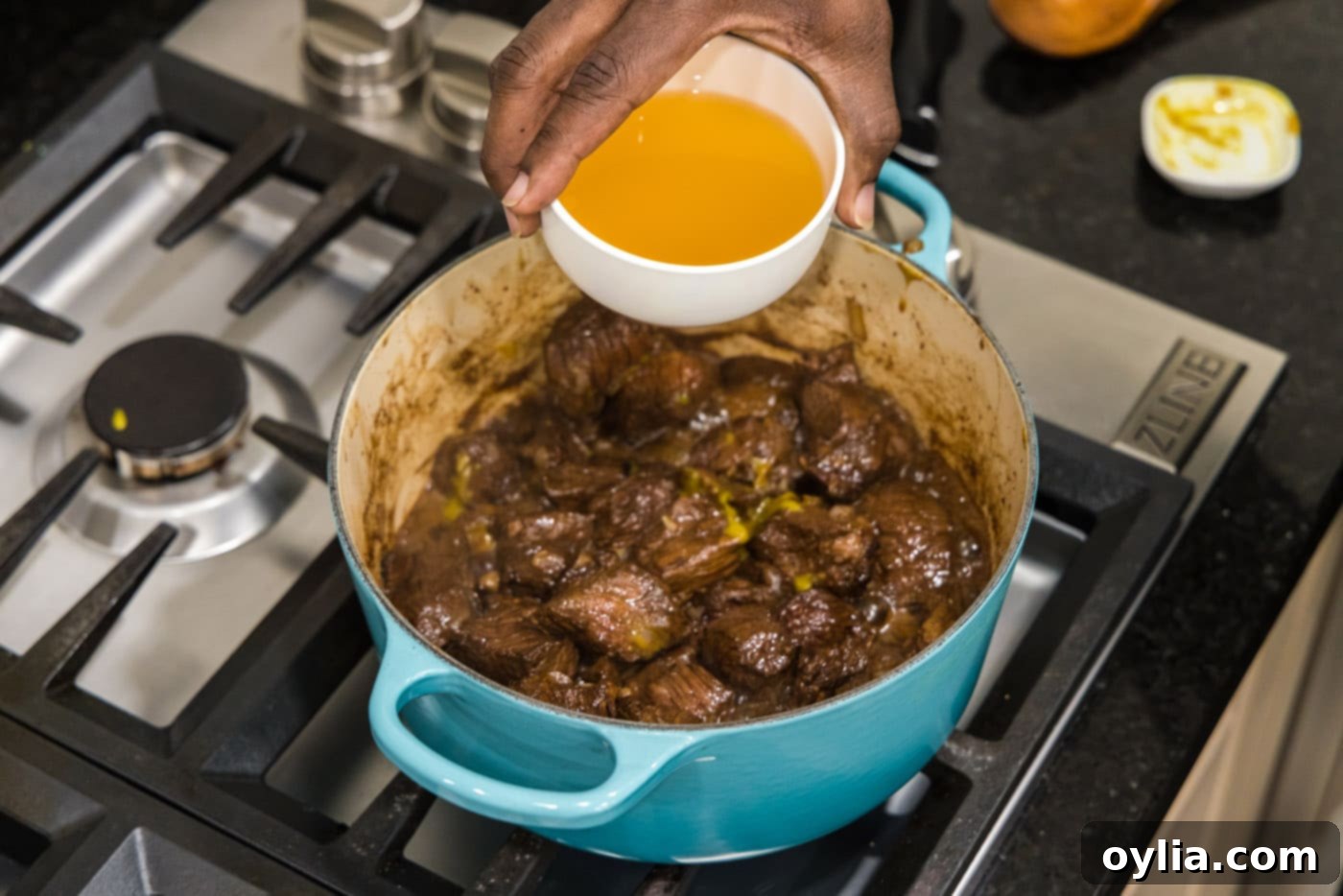 adding chicken stock to beef tips and onions in a pot