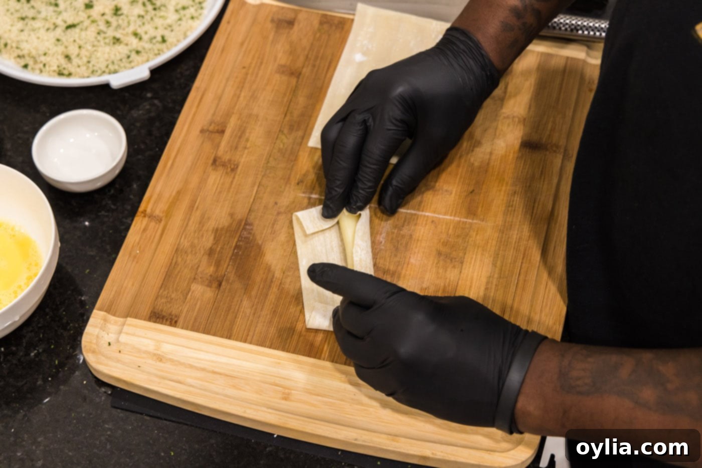 hands rolling a string cheese into an egg roll wrapper