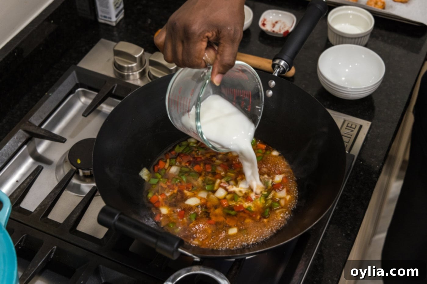 Pouring a cornstarch slurry into the sweet and sour sauce in a skillet with vegetables to thicken it.