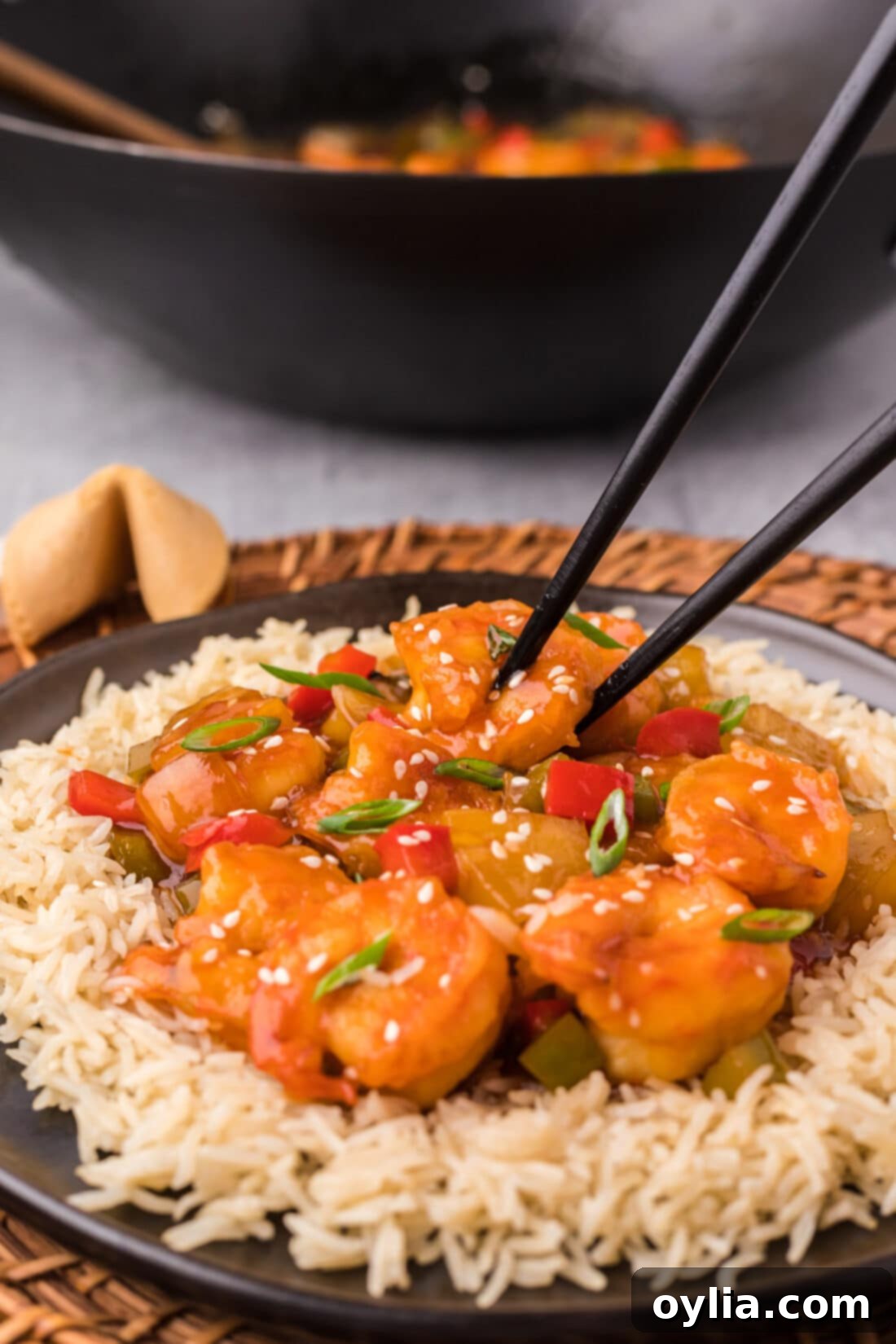Sweet and Sour Shrimp served on a plate over white rice with chopsticks ready to eat.