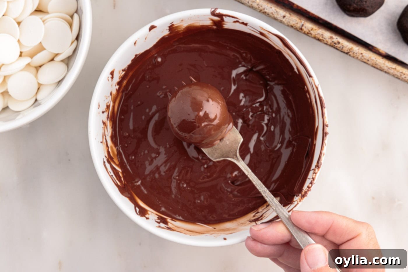 Removing an Oreo truffle from melted chocolate with a fork, tapping off excess.