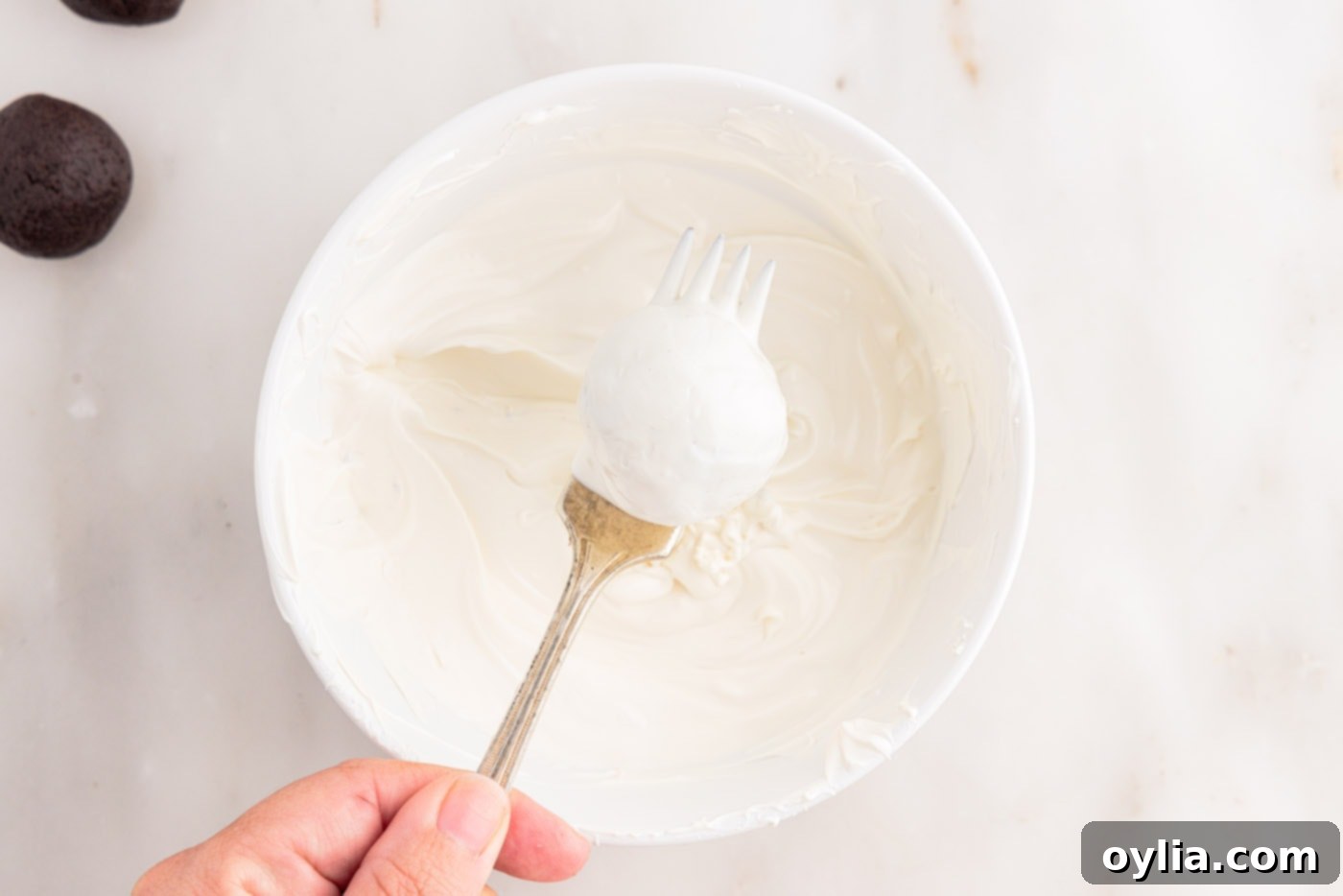 Removing an Oreo truffle from white chocolate with a fork.