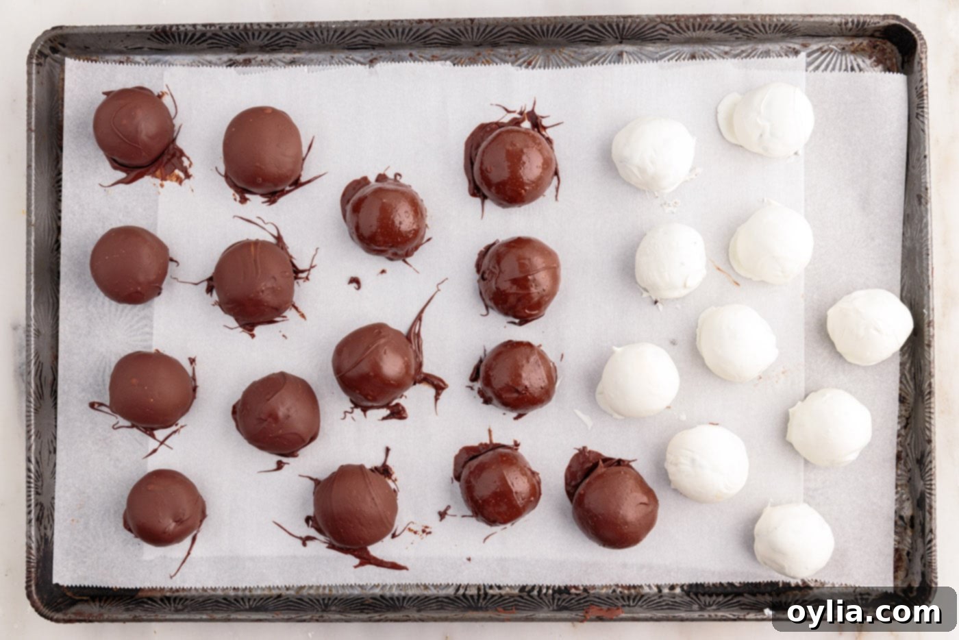 Chocolate-dipped Oreo balls drying on a baking sheet with parchment paper.